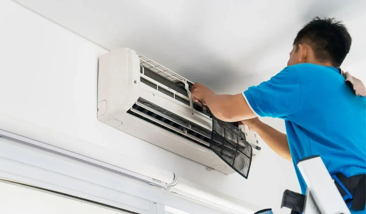 Técnico da Fort Ar Condicionado limpando o filtro de um ar-condicionado split instalado na parede